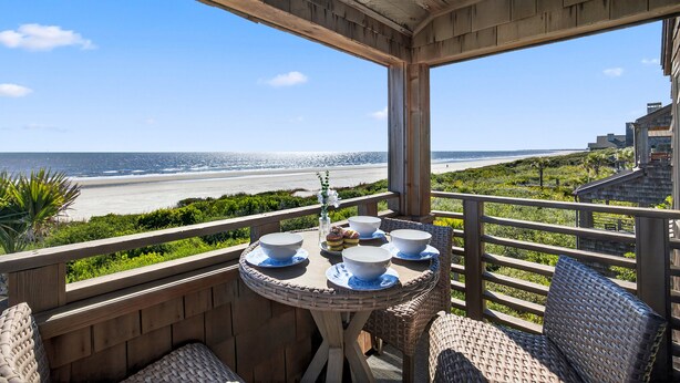 A wooden balcony with a table set for dining, overlooking a beach and ocean.