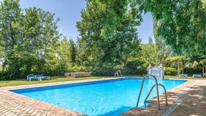 A rectangular swimming pool with a brick border, surrounded by trees and a pergola.