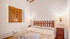 A bedroom with a wooden bed, a window with wooden shutters, two bedside lamps, and a small wooden nightstand.