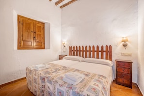 A bedroom with a wooden bed, a window with wooden shutters, two bedside lamps, and a small wooden nightstand.