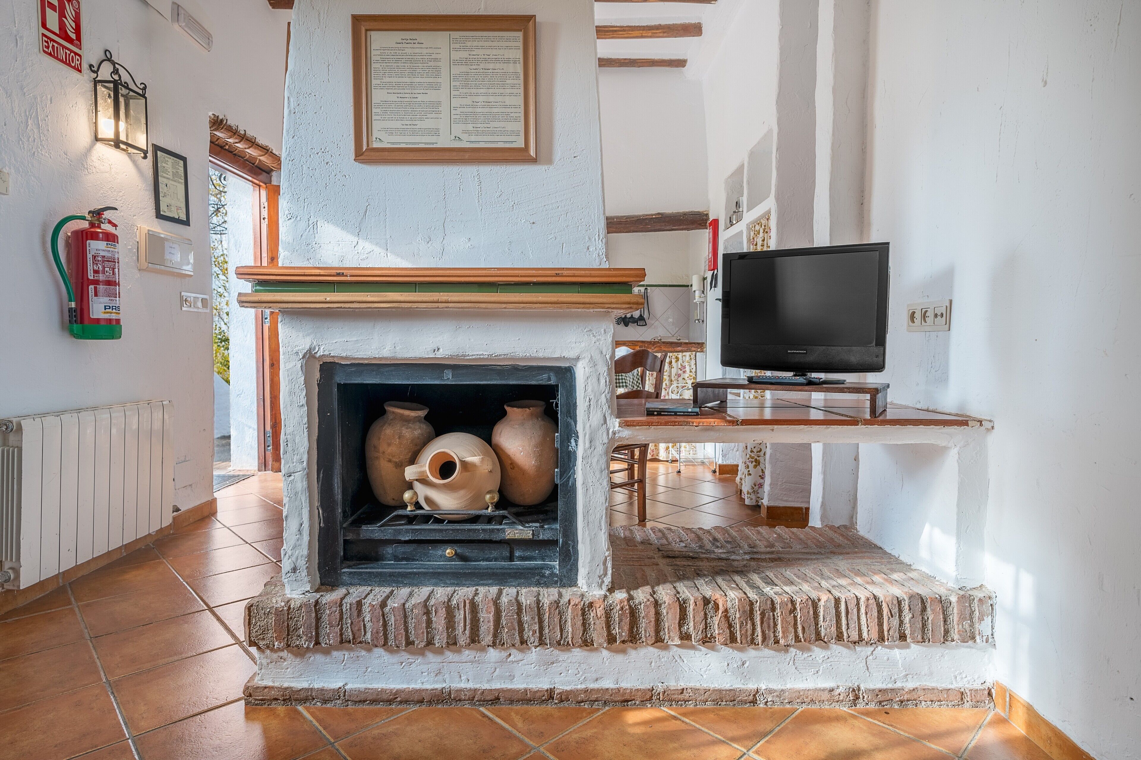 A fireplace with pottery, a television, and a fire extinguisher on the wall.