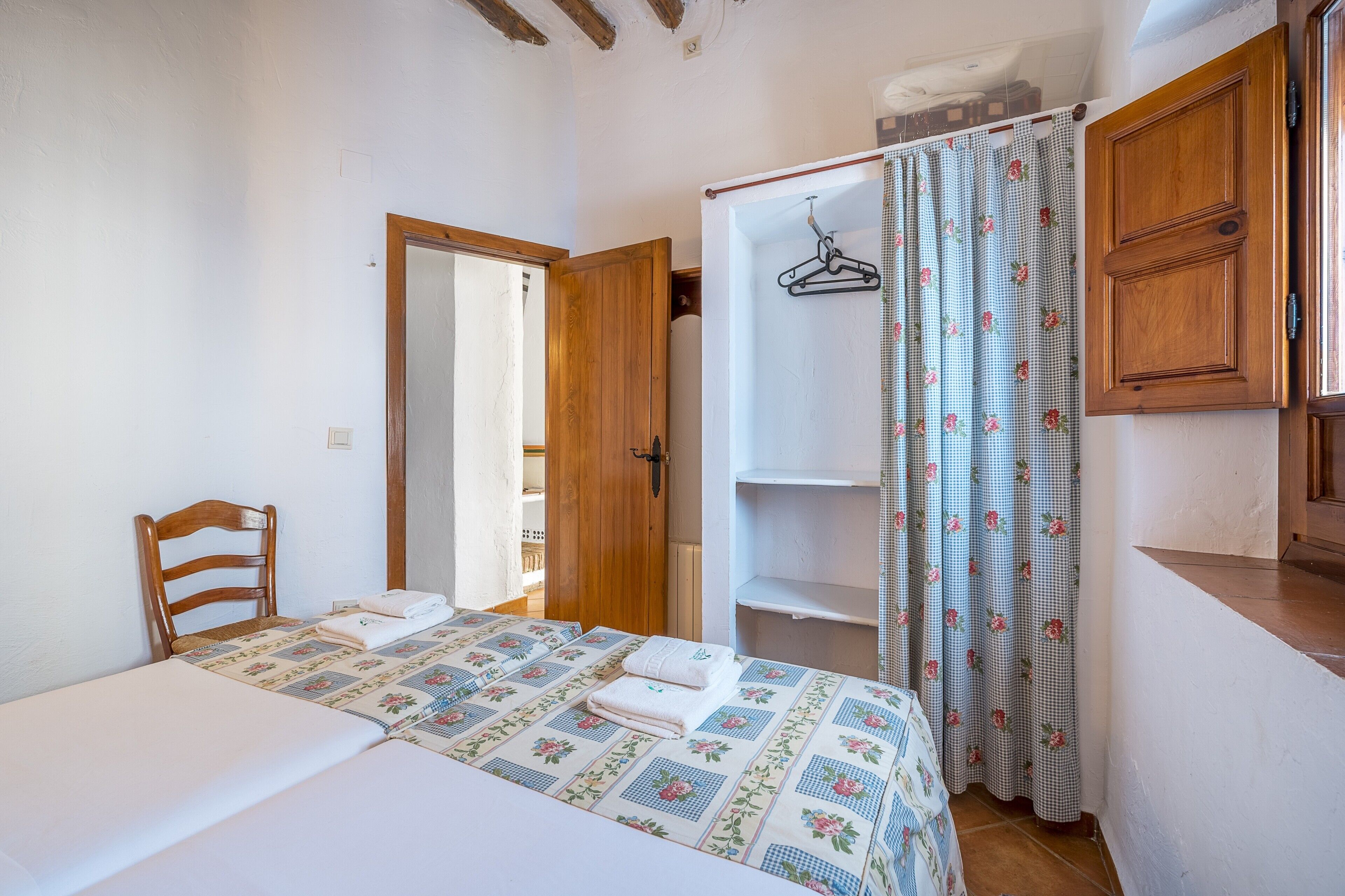 Quarto com cama, uma cadeira de madeira, guarda-roupa e banheiro com cortina de chuveiro.