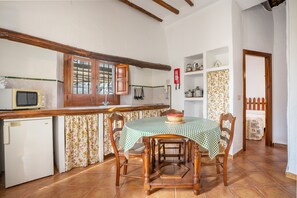 Una cocina con mesa, sillas, microondas, refrigerador y armarios de madera.