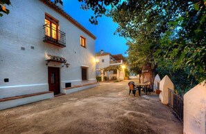 Un patio con un edificio blanco, una puerta de madera y una mesa con sillas.