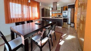 Una cocina moderna con una isla central, electrodomésticos de acero inoxidable y un comedor con una mesa larga y sillas.