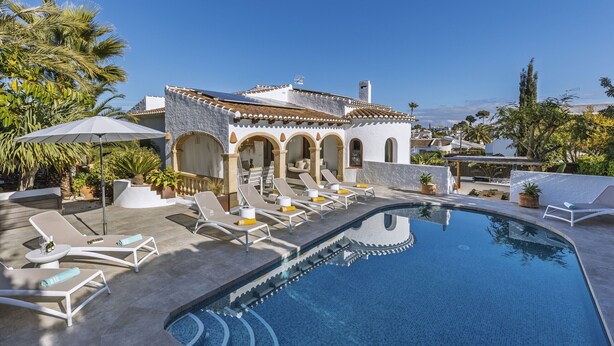 A poolside area with lounge chairs and a clear blue pool, surrounded by a building with arches and a tiled roof. - Villa Artista (Javea / Xàbia)