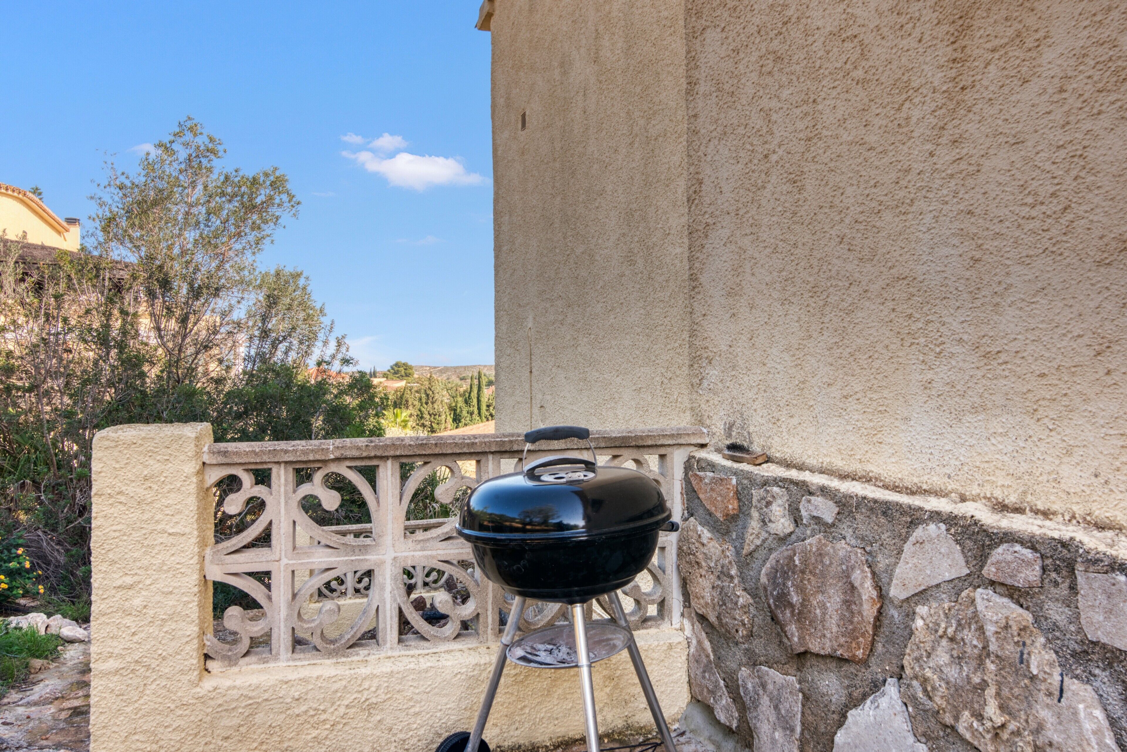 Een barbecue op een balkon met een stenen muur en decoratief hekwerk.