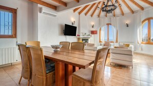 Un coin repas avec une table en bois et des chaises en osier, un téléviseur à écran plat fixé au mur et une cheminée.