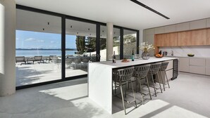 A modern kitchen with a large island, bar stools, and a view of the sea.