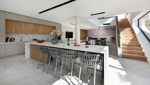 A modern kitchen with a central island, bar stools, and a staircase leading to an upper level.