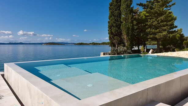 A rectangular infinity pool with clear blue water, surrounded by a stone deck.
