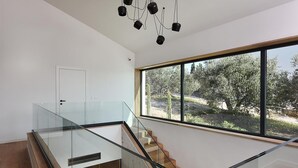 A modern interior with a glass staircase, a large window with a view of trees, and a minimalist design.