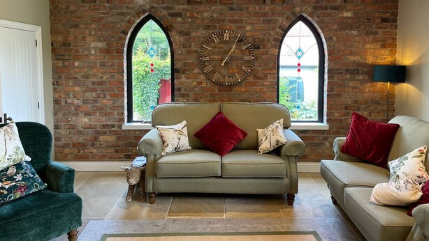 A living room with a brick wall, two windows, a sofa, and a chandelier. - Littlemount Farm Cottage (Enniskillen)
