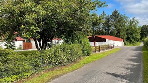 A rural road with a barn and a white building with a red roof. - Littlemount Farm Cottage (Enniskillen)