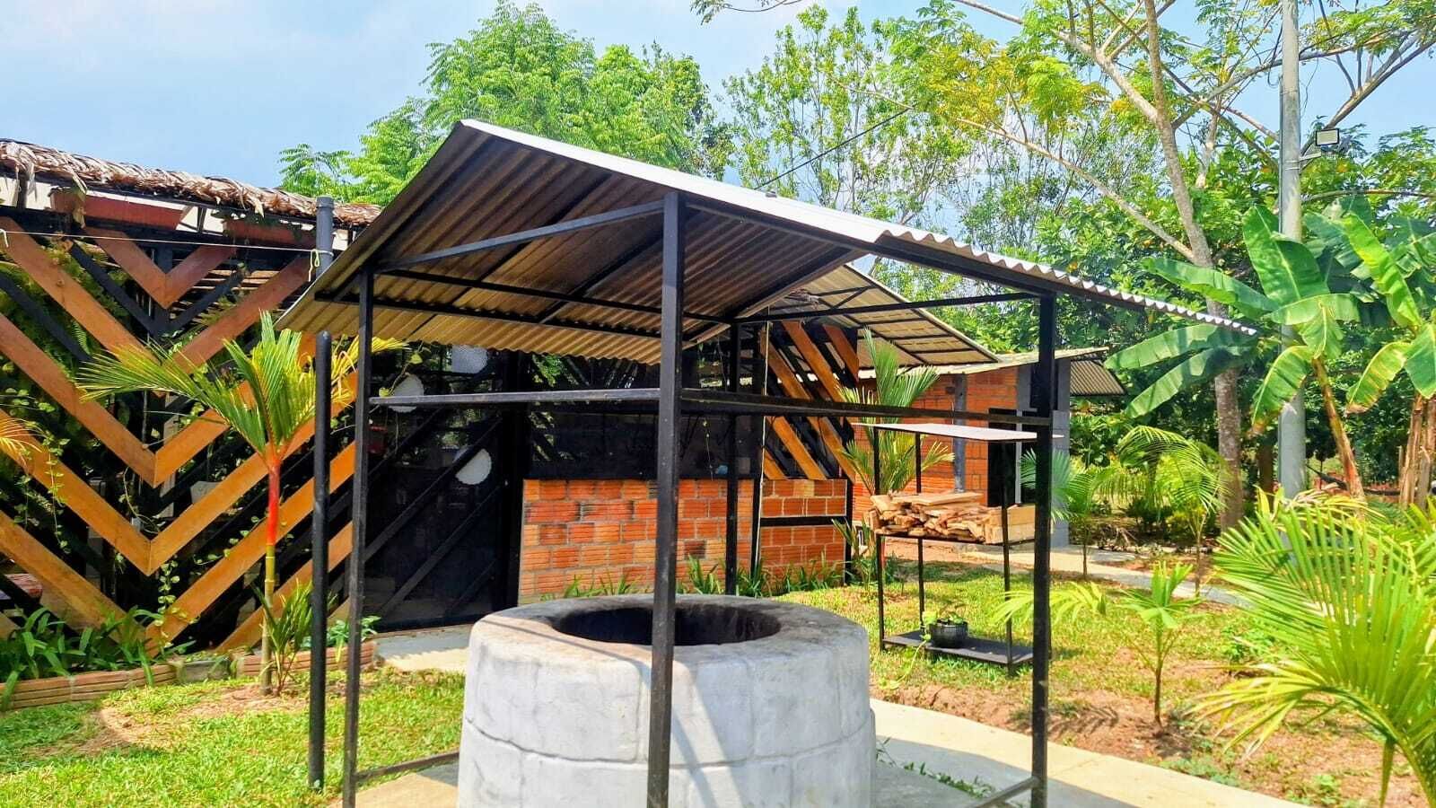 Un espace extérieur abrité, doté d’une structure en briques, d’un barbecue en métal et d’un puits en béton.