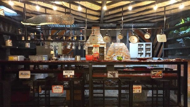 Zona de bar con horno de ladrillo, luces colgantes y taburetes con nombres de bebidas.