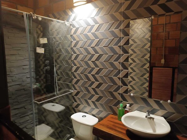 Ein modernes Badezimmer mit Fischgrätmusterfliesen, einer Duschkabine aus Glas, einem Holzbadezimmermöbel und einem großen Spiegel.