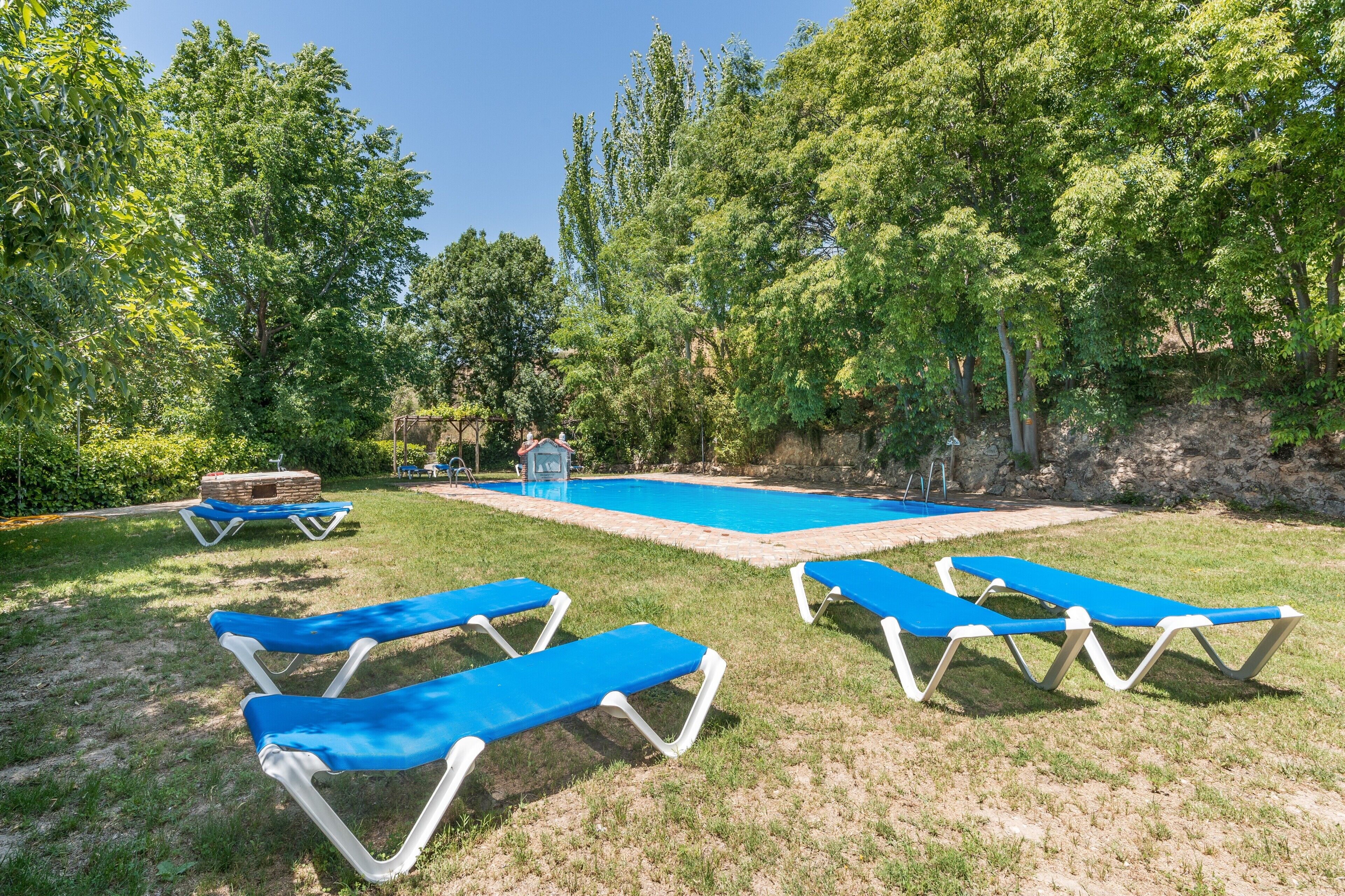 A pool area with blue lounge chairs, a stone structure, and trees.