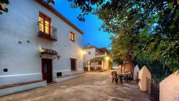 A courtyard with a white building, a wooden door, and a table with chairs. - Apartment 'Apartamento La Cuadra' with Mountain Views, Shared Pool, and Wi-Fi (La Zubia)