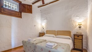 A bedroom with two beds, a window with bars, a wooden ceiling beam, and two wall-mounted lamps. - Apartment 'Apartamento La Cuadra' with Mountain Views, Shared Pool, and Wi-Fi (La Zubia)