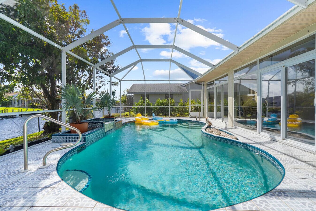 A covered swimming pool with a glass enclosure, surrounded by a tiled deck and potted plants.