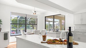 A modern kitchen with a large island, white cabinetry, and a view of the outdoors.