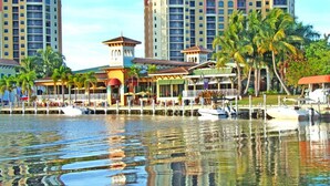 A waterfront hotel with multiple buildings, a dock with boats, and palm trees.