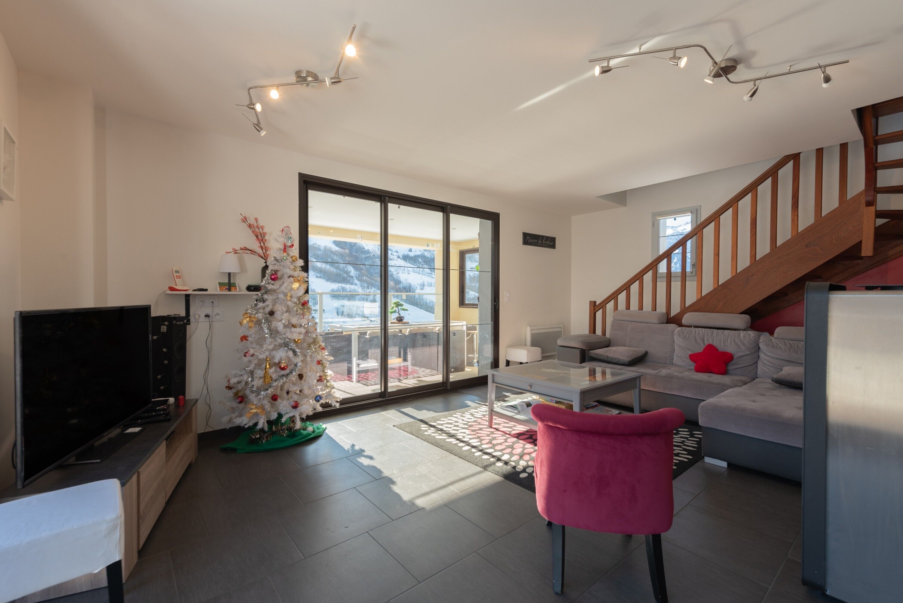 A modern living room with a television, a Christmas tree, a sofa, and a staircase.