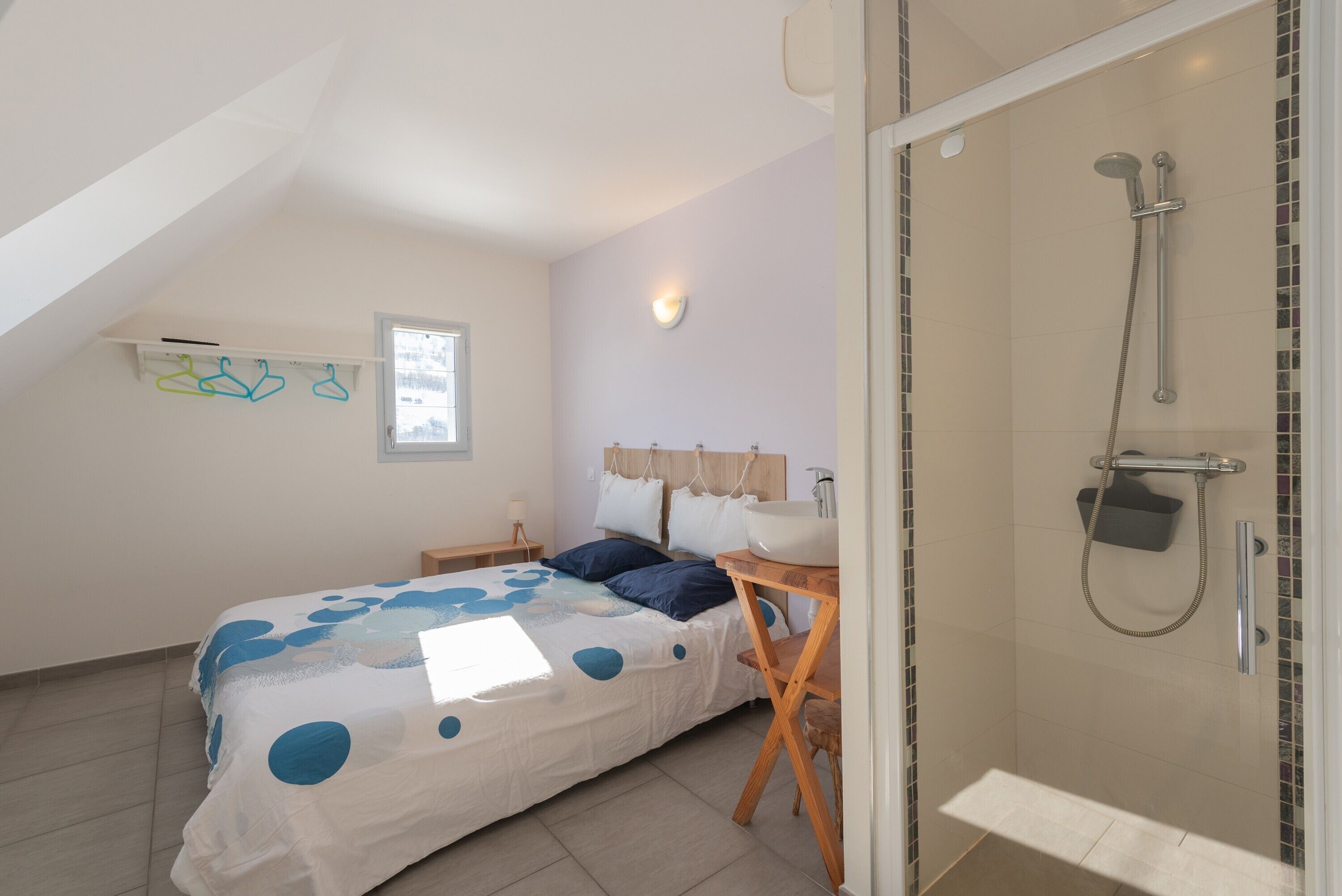 Ein Schlafzimmer mit Bett, Nachttisch, Fenster, Dusche und Handtuchhalter.