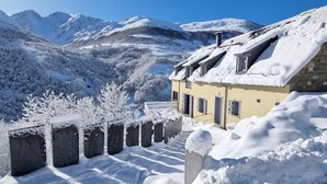 Un refugi de muntanya amb un teulat cobert de neu, parets de pedra i vistes a muntanyes nevades.