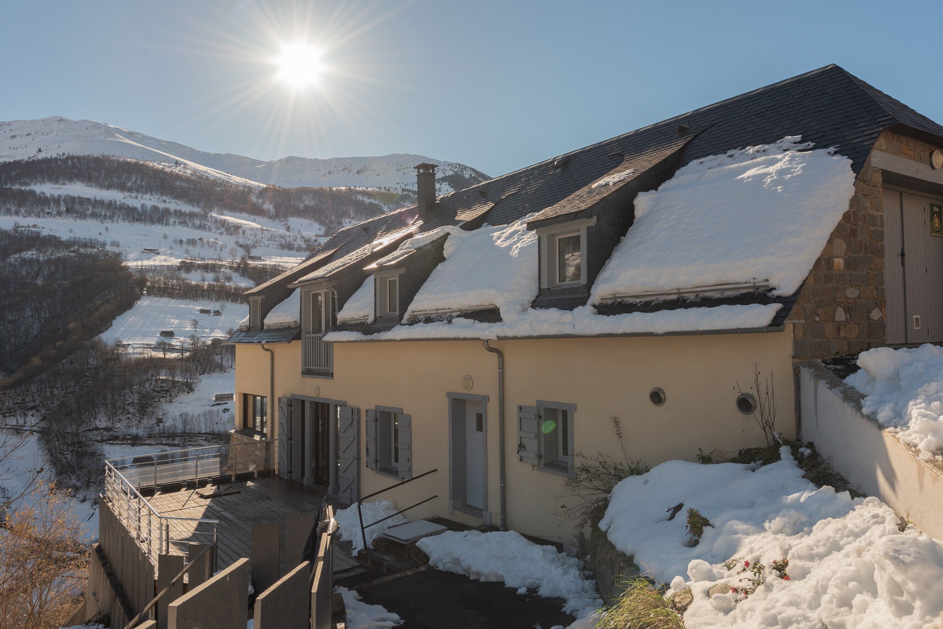 Una casa con techo inclinado, un pequeño porche y vistas de montañas nevadas.