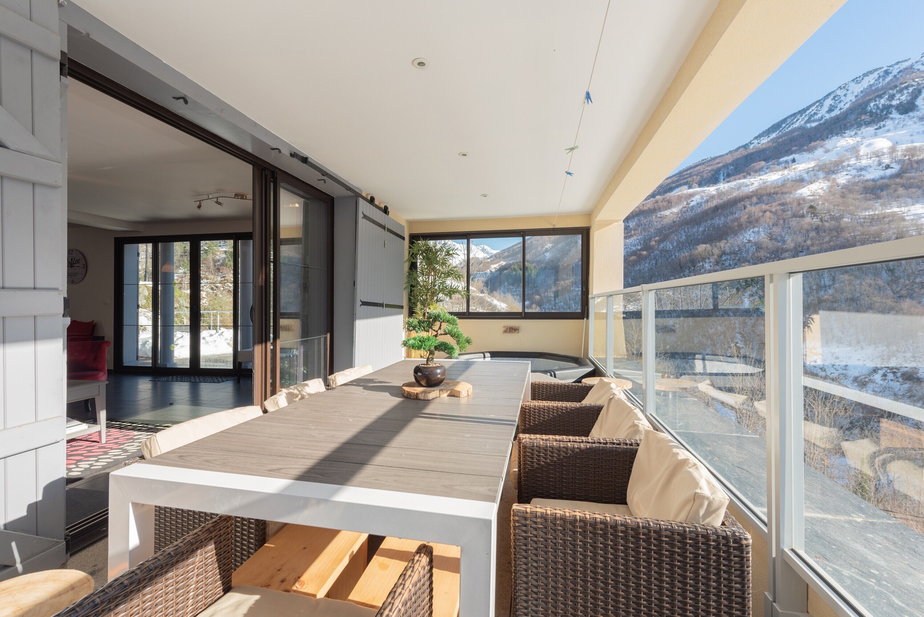 Un intérieur moderne avec une grande table à manger, des meubles en osier et une vue sur une montagne enneigée.