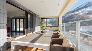 Un intérieur moderne avec une grande table à manger, des meubles en osier et une vue sur une montagne enneigée.