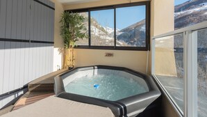 Banyera d'hidromassatge amb vista a muntanyes nevades, una planta en test i una porta corredissa.