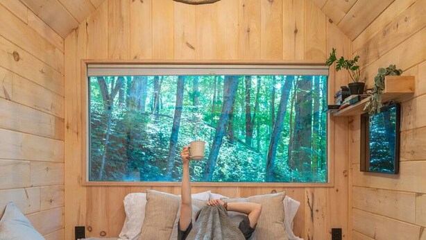 Ein Schlafzimmer in einer Holzhütte mit einem großen Bett, Blick auf einen Wald durch ein Fenster und einer Chandelier.