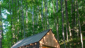 Eine rustikale Holzhütte mit Veranda und zwei Stühlen, umgeben von einem Holzzaun und Bäumen.