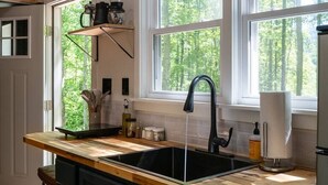 Eine Küche mit einer Holzausziehtafel, schwarzen Schränken, einer schwarzen Spüle und einem Fenster mit Blick auf Bäume.