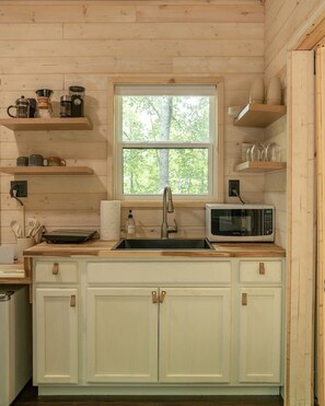 A kitchen with wooden cabinets, a stainless steel sink, a microwave, and shelves with kitchenware.