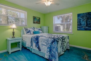 A bedroom with a bed, a nightstand, a lamp, and two windows with blinds.