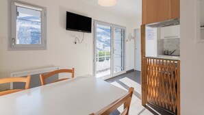 A modern kitchen with a TV, wooden cabinets, and a view of snowy mountains through the glass door. - Chalet "De Sers" with Mountain Views, Private Terrace and Wi-Fi (Sers)