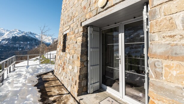 A stone building with a glass door, a metal railing, and a snowy mountain backdrop. - Chalet "De Sers" with Mountain Views, Private Terrace and Wi-Fi (Sers)