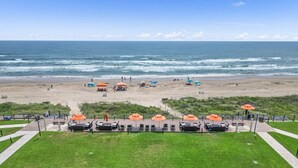 Een strand met parasols en ligbedden, een pad dat naar het strand leidt en uitzicht op de oceaan.
