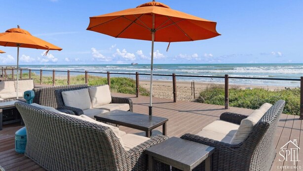 Een terras met rieten meubels en oranje parasols met uitzicht op een strand.