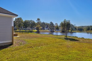 A grassy area with a small pond, a white building, and trees in the background.