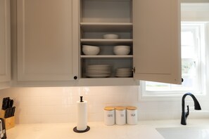 A kitchen with white cabinets, a white countertop, a black faucet, and three jars labeled coffee, tea, and sugar.