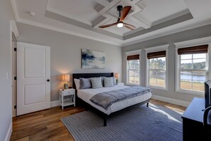 A bedroom with a bed, nightstands, a ceiling fan, and large windows with views of a lake. - Newly Built, Stunning 4BR/2BA with Waterfront Views (Thomasville)