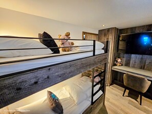 A bunk bed room with a television on the right and a wooden wall.