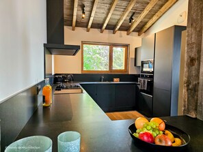 A modern kitchen with a large island, a window, and a view of greenery outside.