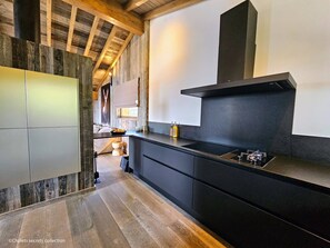 A modern kitchen with a sleek black countertop, wooden flooring, and a large black range hood.