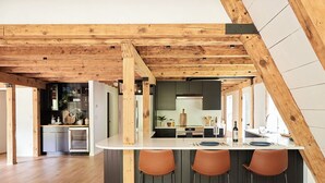 Une cuisine moderne dotée d’un îlot central, de tabourets de bar et de poutres en bois au plafond.